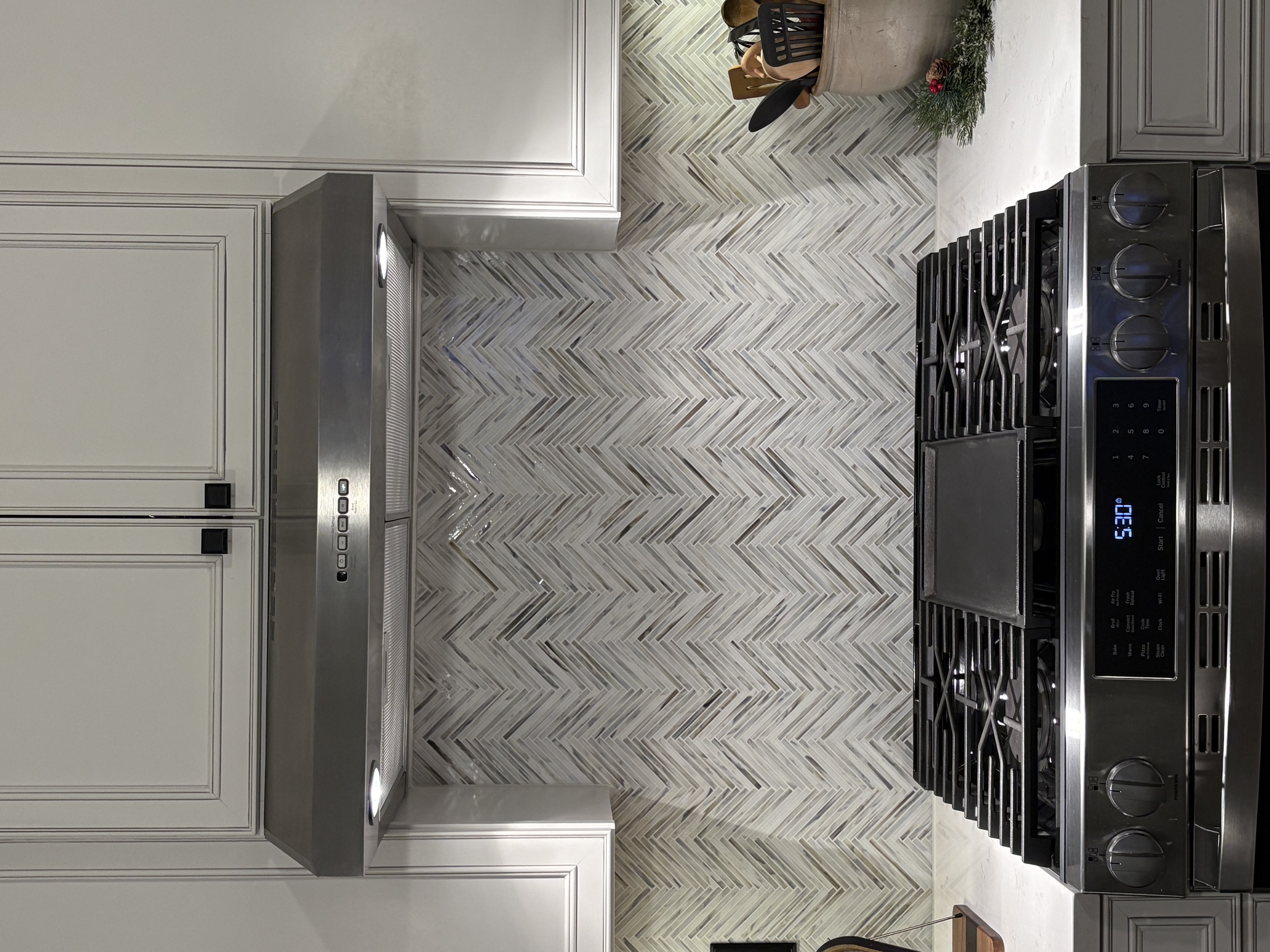 The center view of a kitchen with a white tile backsplash showing the stove and range hood